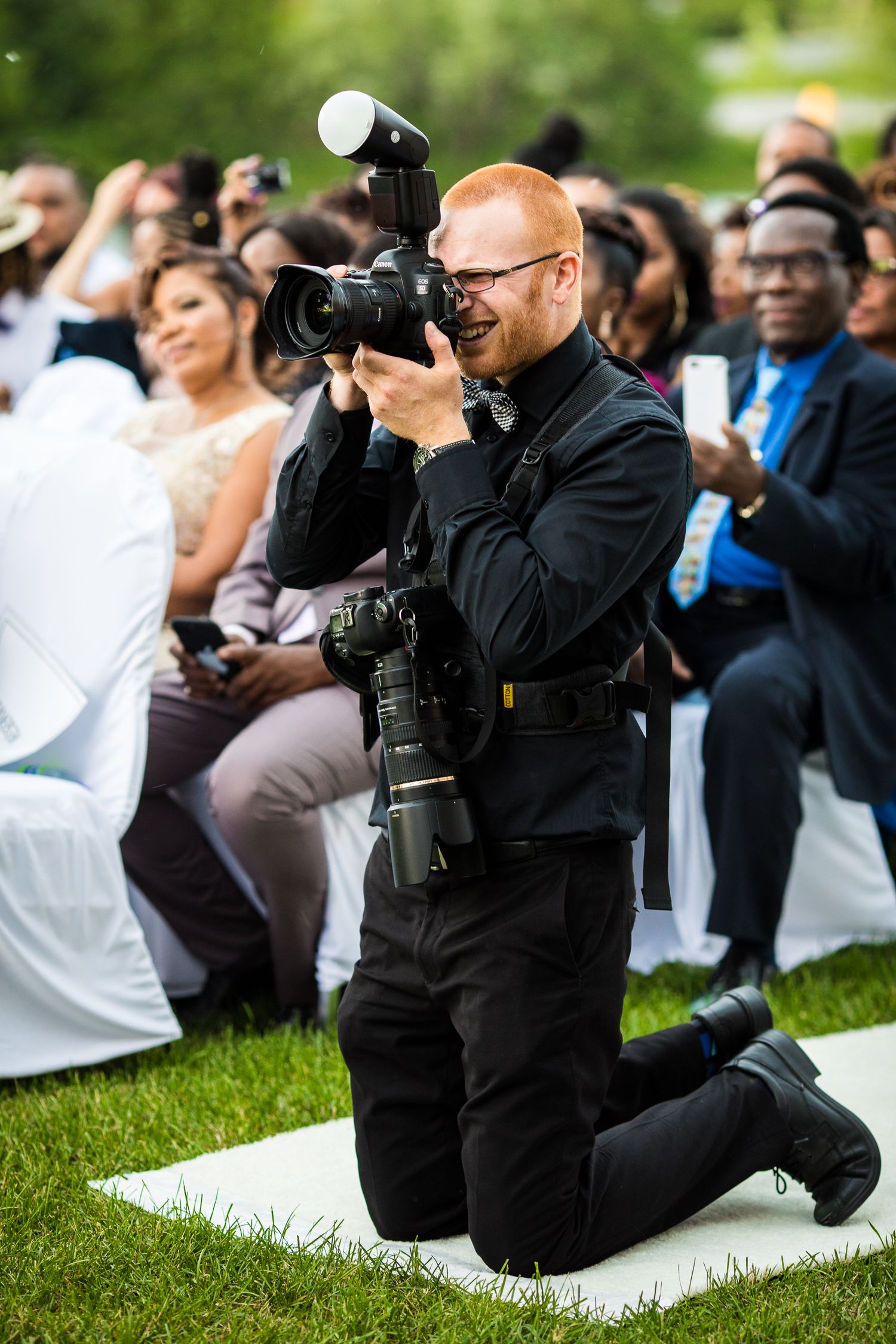 Photo du photographe Brophoto en plein travail durant un mariage. Tout vêtu de noir, il est à genou et photographie la cérémonie.