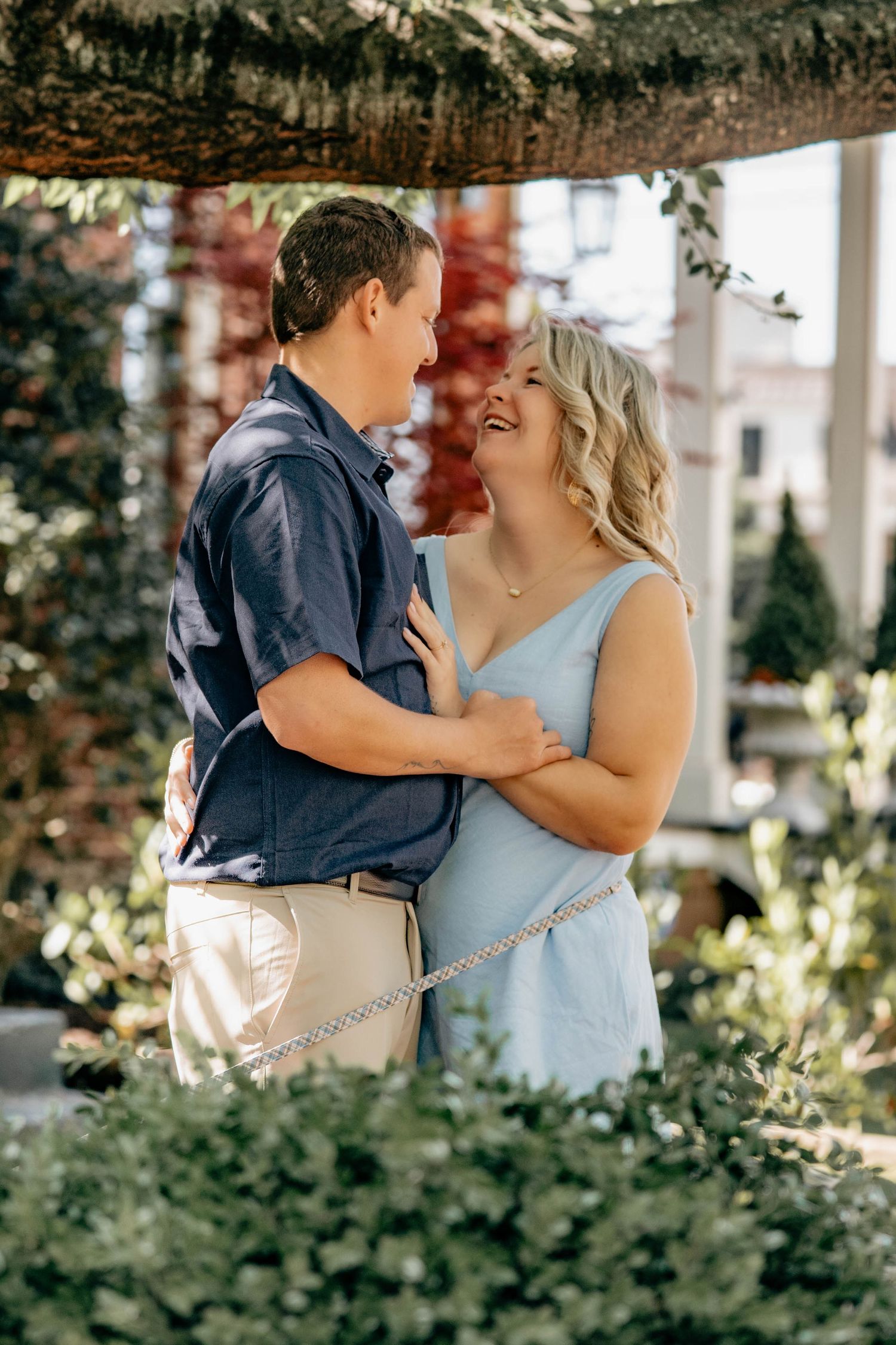 A couple shares a joyful moment together in a garden setting, with the woman wearing a light blue dress and man in navy.