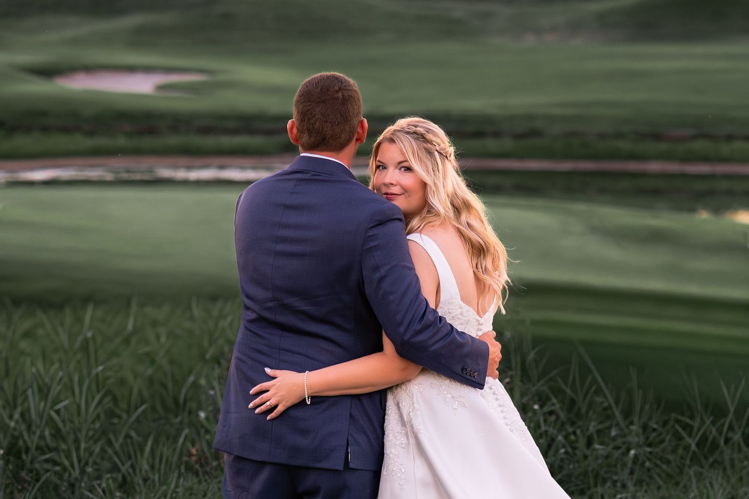 A couple in wedding attire embraces while walking through a lush green golf course on their special day.