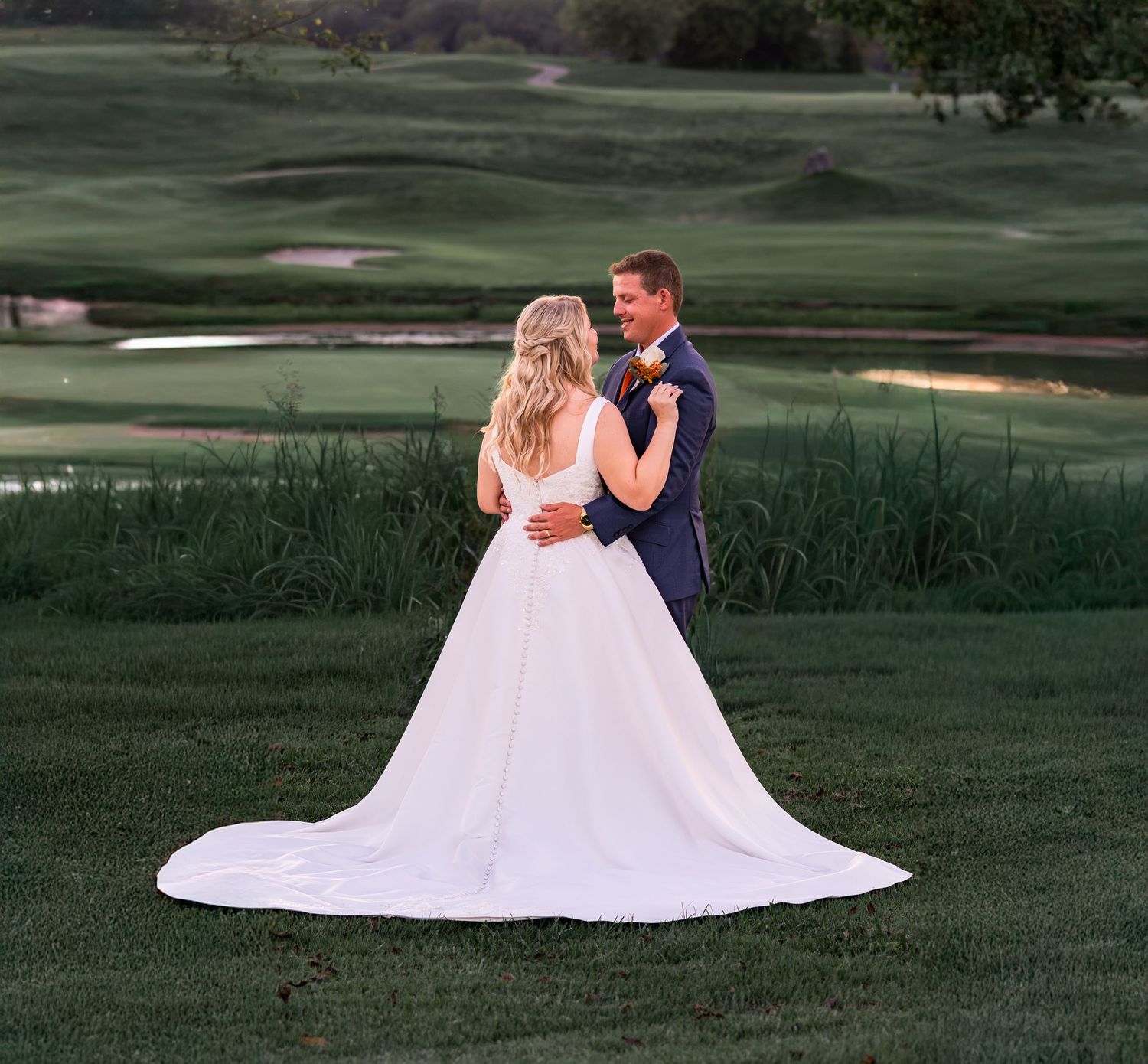 A romantic couple in wedding attire shares an intimate moment on a lush golf course at sunset.