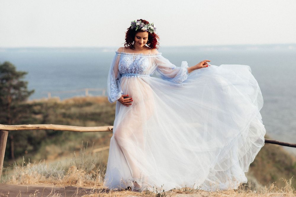 Person in flowing white dress twirling on coastal clifftop at sunset.