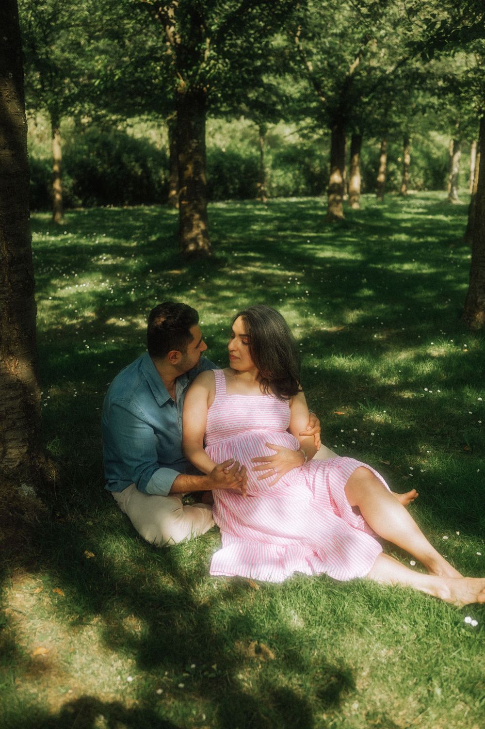 A tender moment between a couple relaxing on grass in a sunlit park.