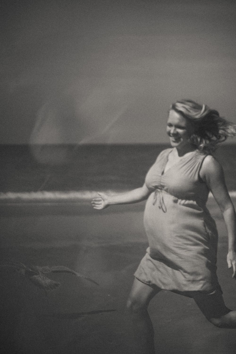 Black and white photo of woman dancing joyfully on beach in flowing dress.