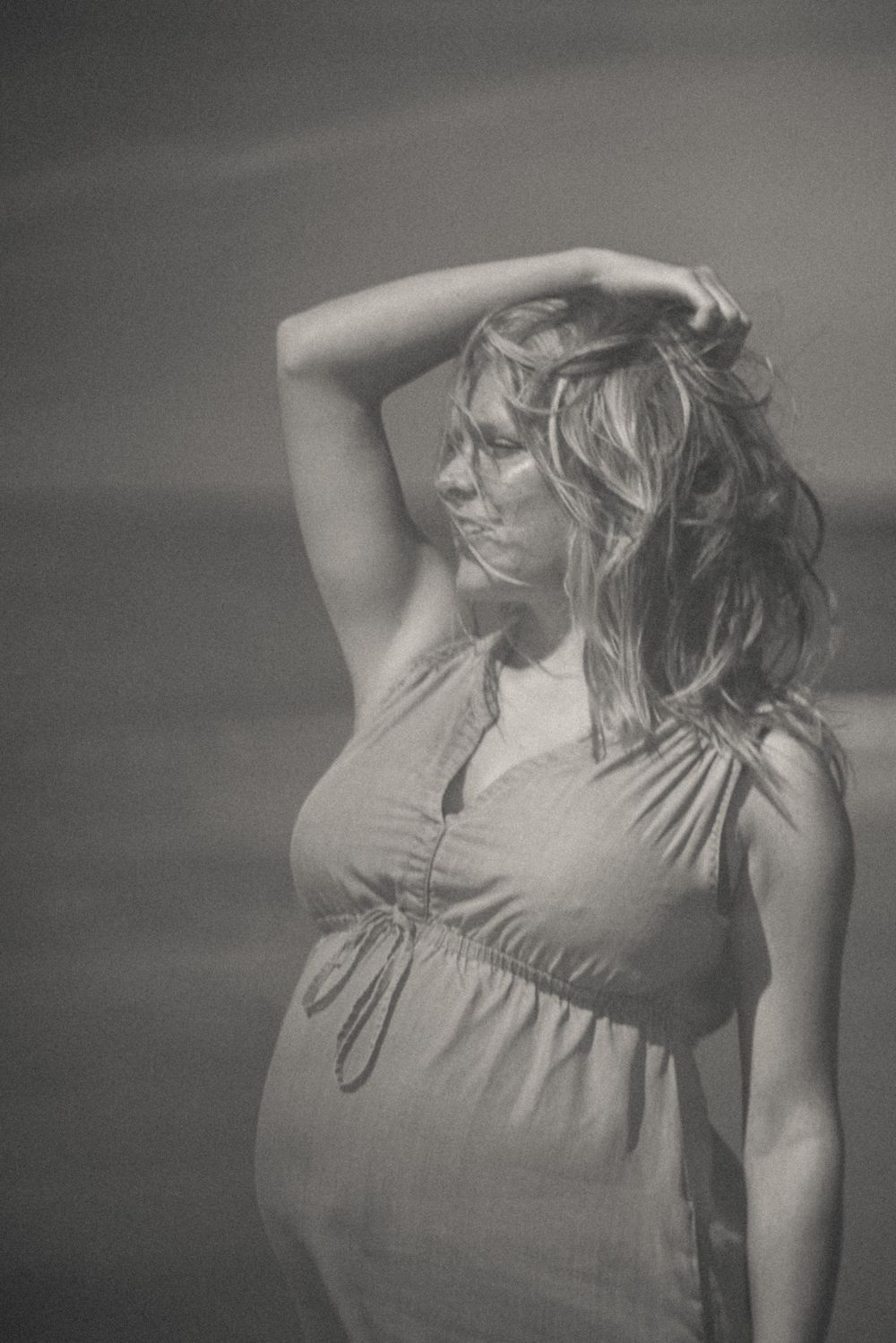 Artistic black and white portraits of woman in gray dress against moody sky.