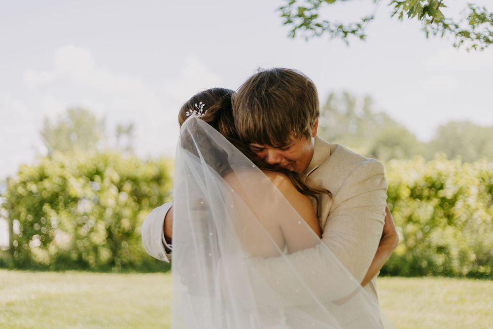 A romantic couple in wedding attire embraces in a sunlit garden setting.