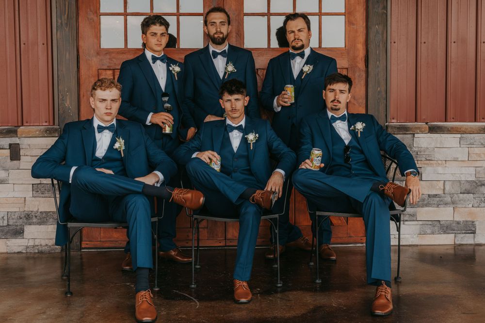 Groomsmen in navy suits and bow ties pose formally in two rows.