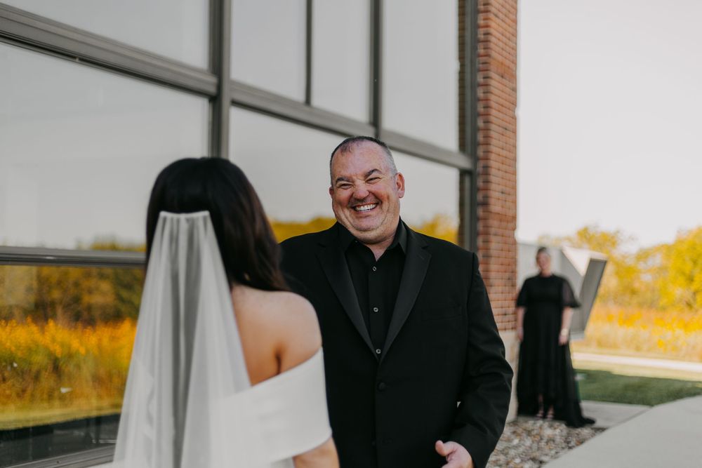 A joyful moment captured during a wedding ceremony as someone in black attire smiles warmly at the bride.