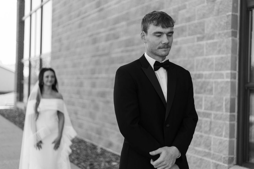 Black and white wedding photo showing first look moment between couple against brick wall.