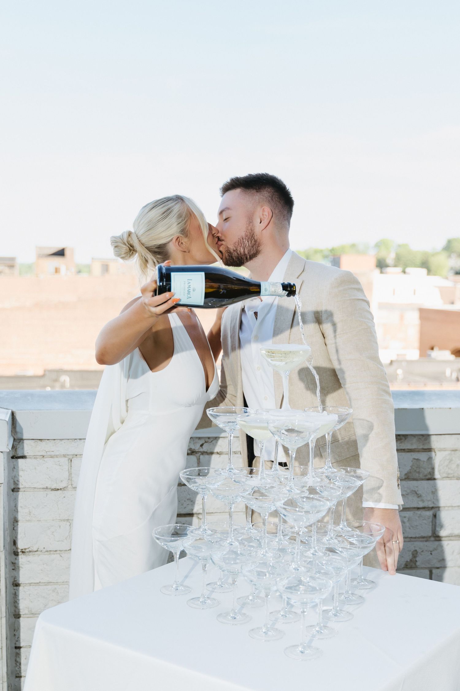Couple pouring champagne into a tower of glasses on their wedding day.