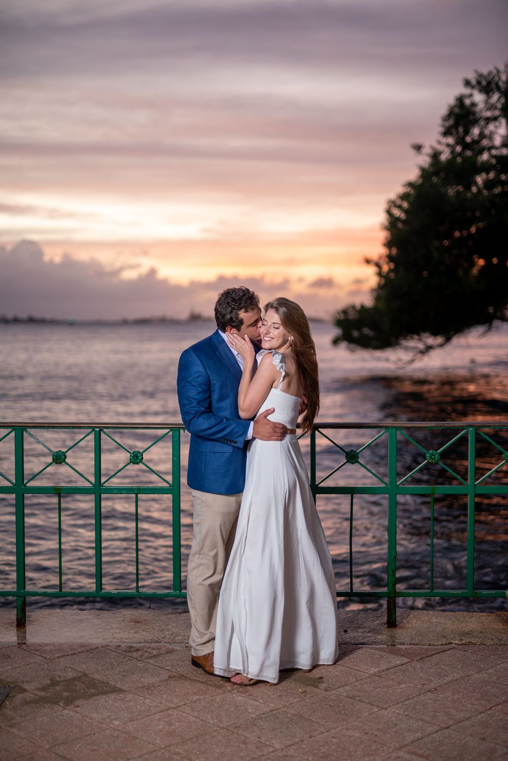 A romantic sunset moment by the ocean with a turquoise railing and pink sky.