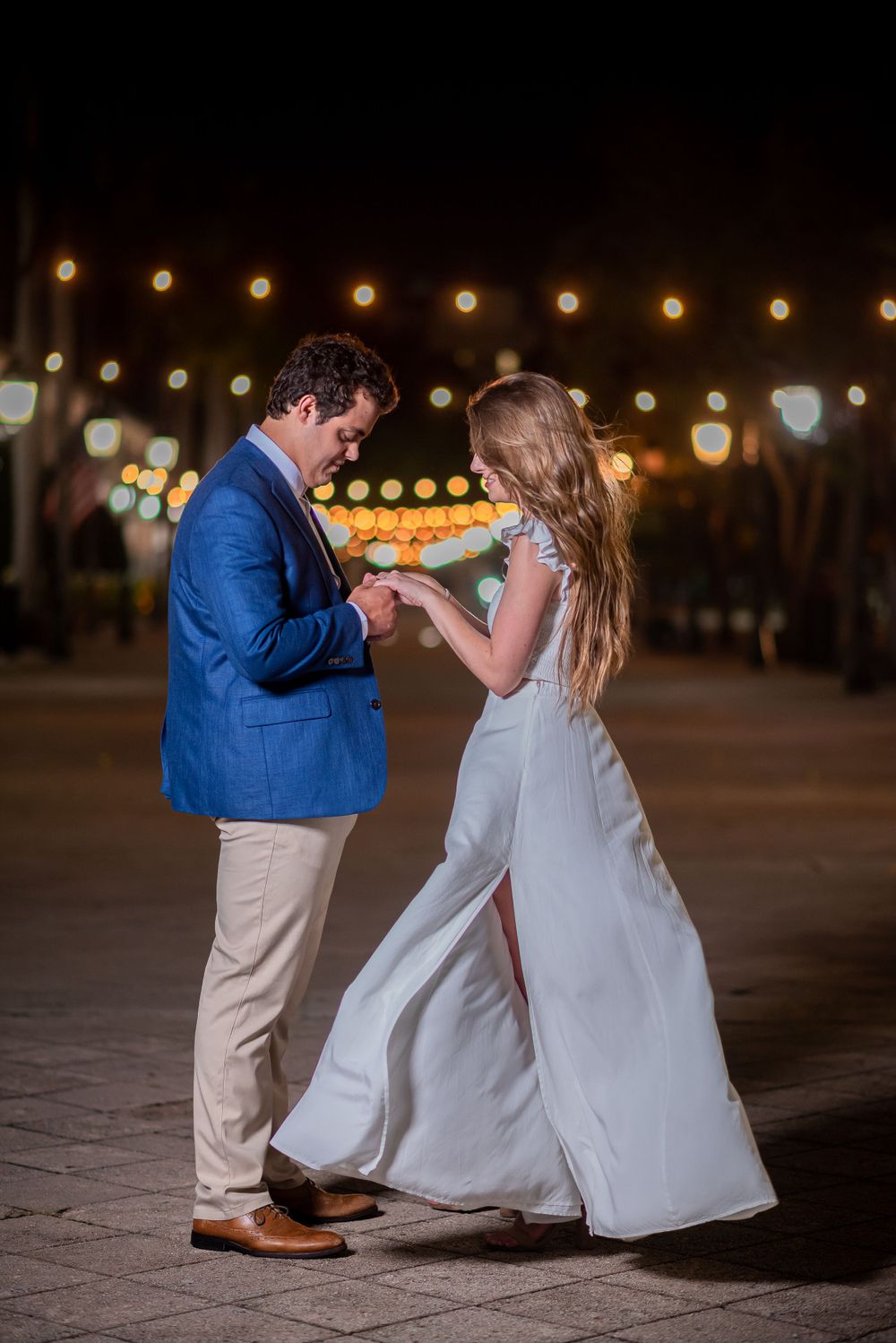 A couple dancing under string lights at night in formal attire.