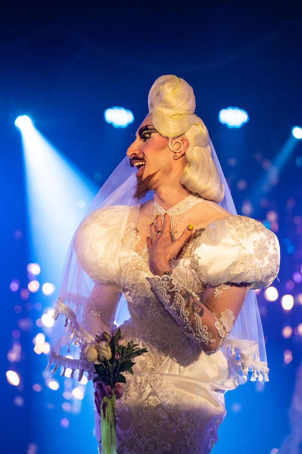 event photography of a drag drag queen in a competition drag pageant in Brighton wears a wedding dress with blonde beehive hair