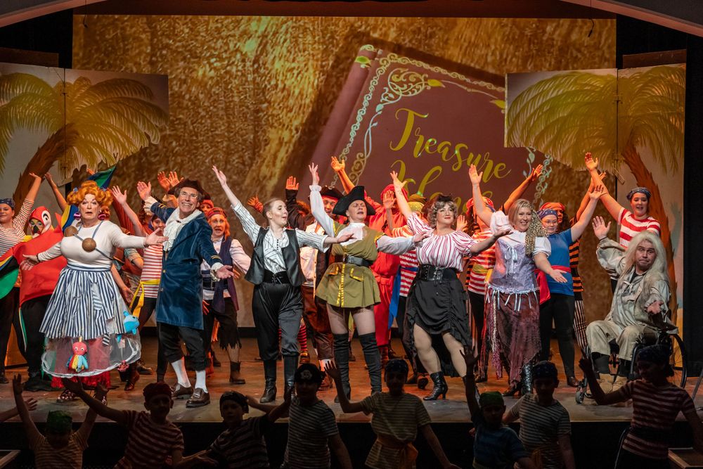 theatre photography of a group of actors on stage for treasure island show all in costume with thierhands raised