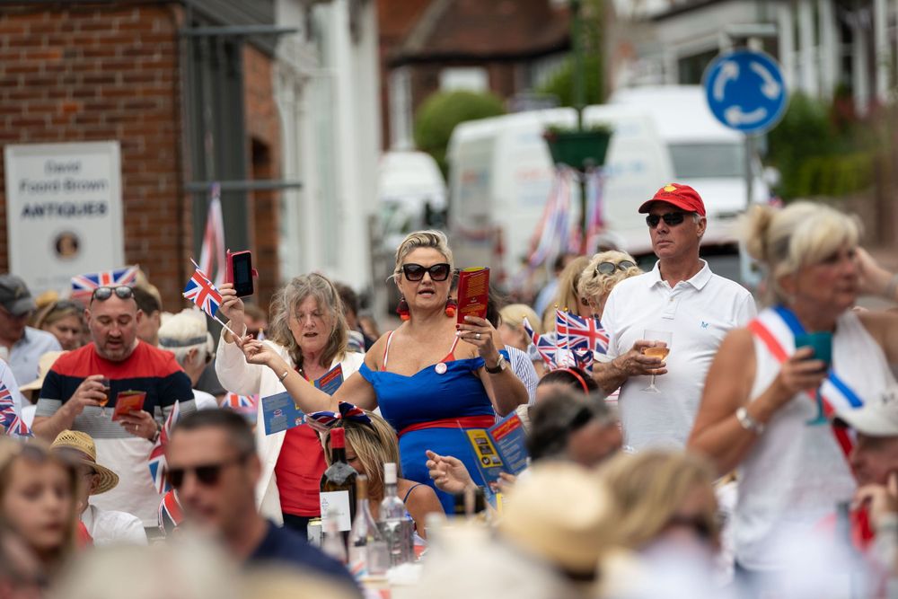 event photography Brighton of a women in union jack dress at a street party she waves a union jack flag with the street party eating and par