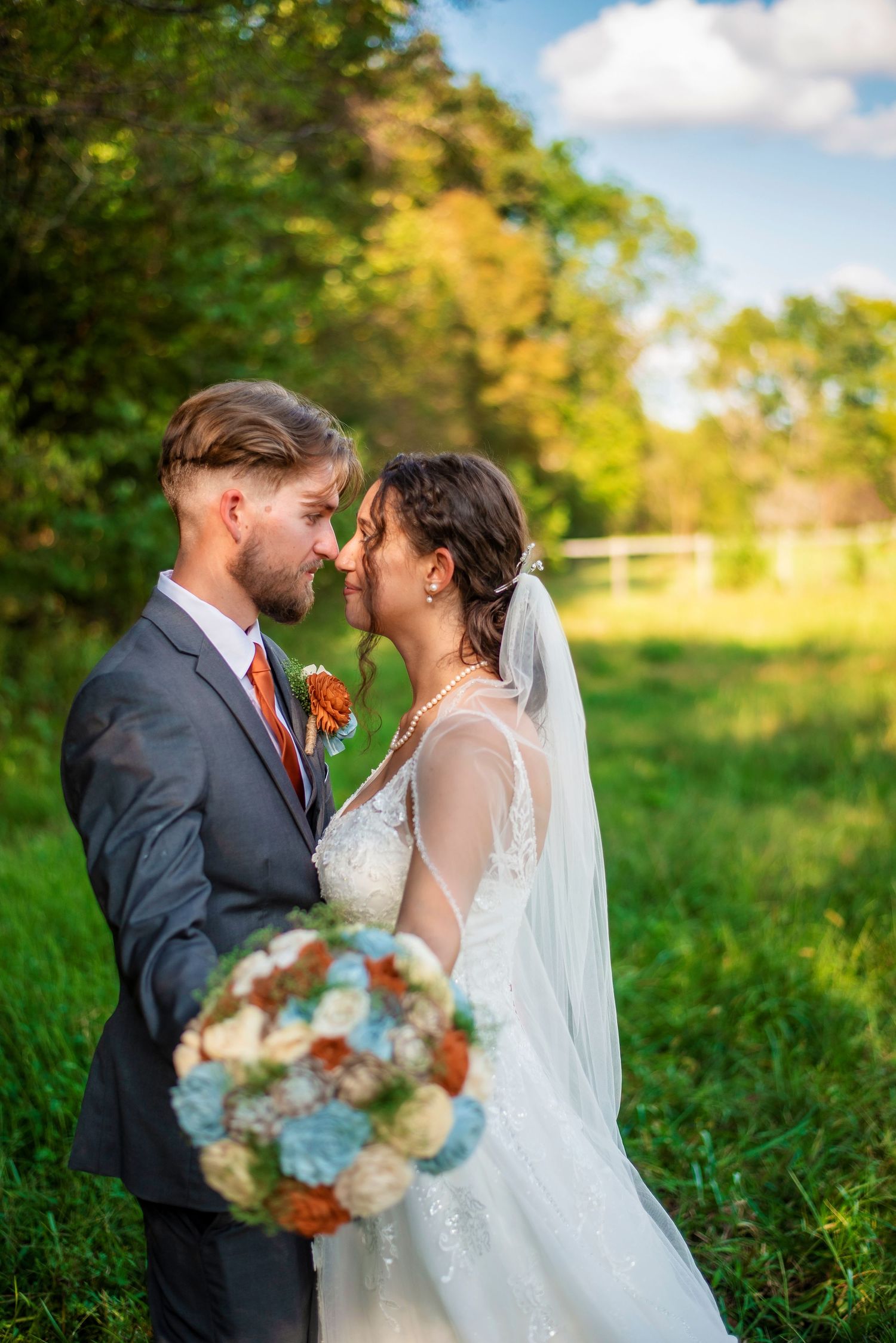 Romantic outdoor wedding photo with couple embracing amid fall foliage.