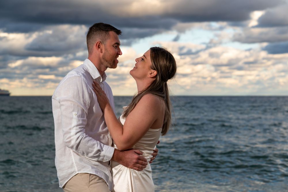 Elopement couple embracing on a Fort Lauderdale beach at sunset, looking at each other with ocean waves and dramatic clouds in the back