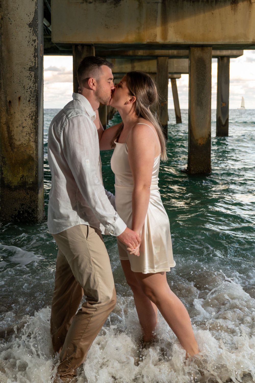 Married couple embracing on a Fort Lauderdale beach at sunset, looking at each other with ocean waves and dramatic clouds in the background