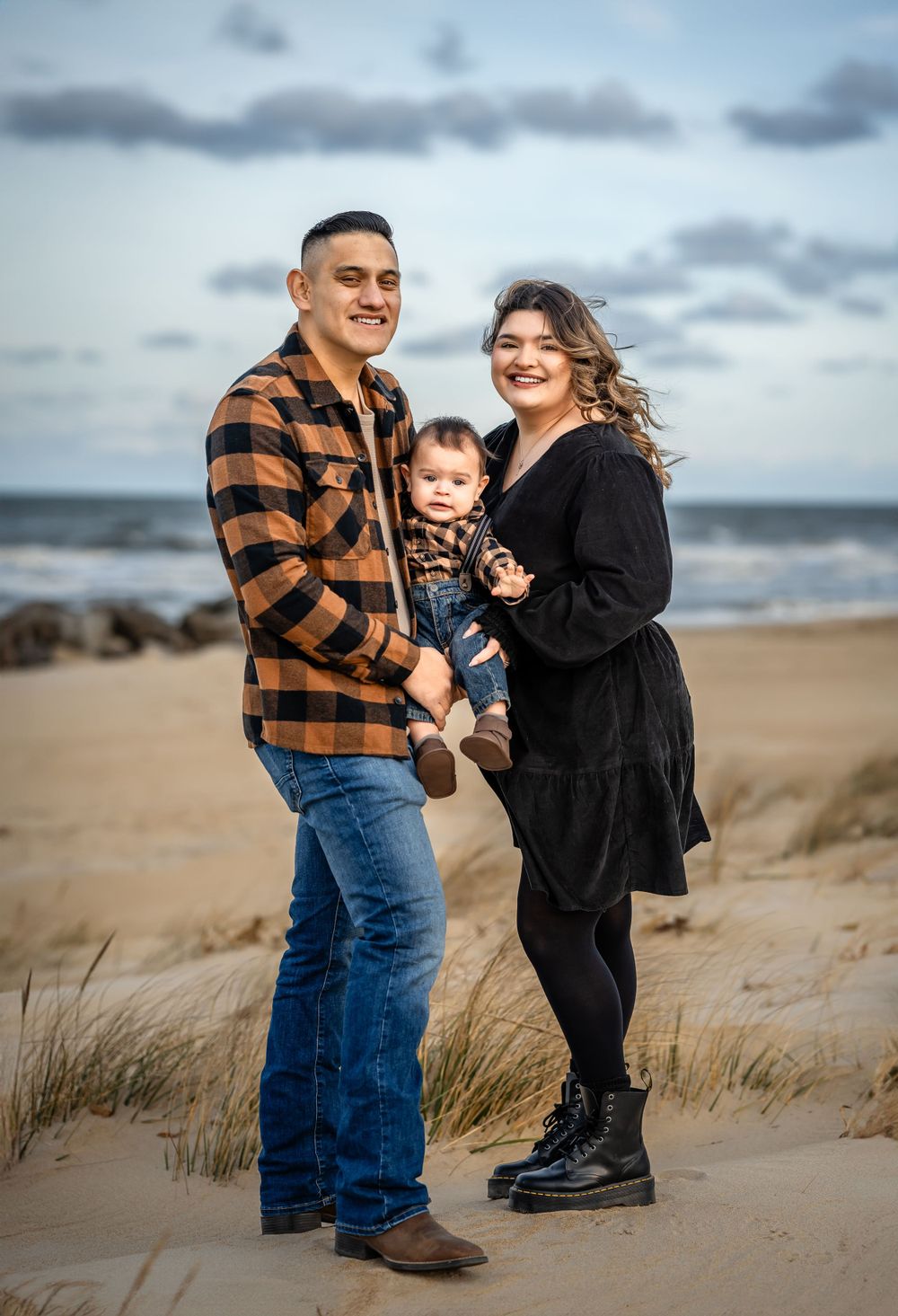 A family poses together on a sandy beach with rocky coastline and moody clouds in the background.