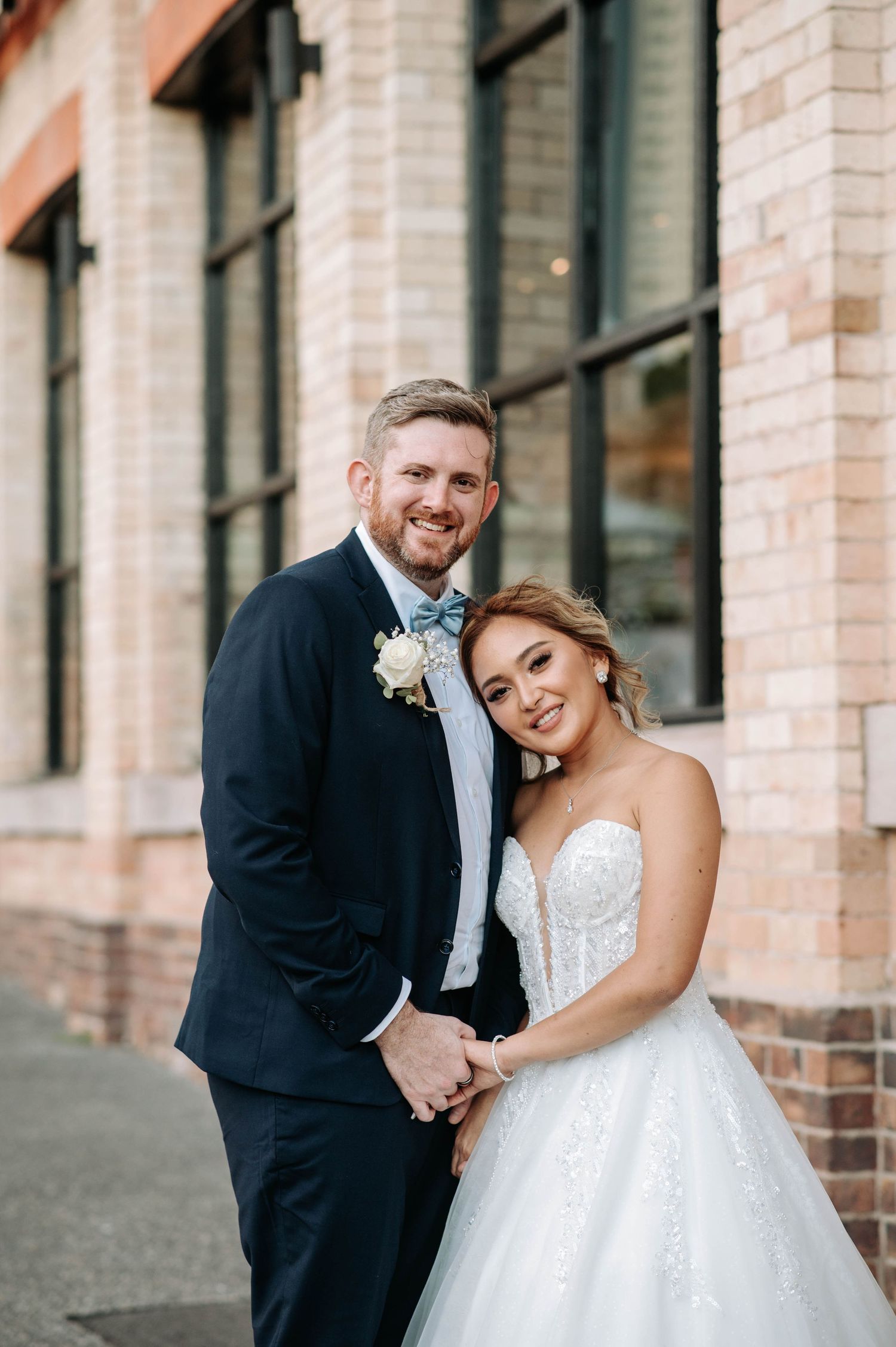 A romantic wedding portrait of a couple in formal attire against a brick building.