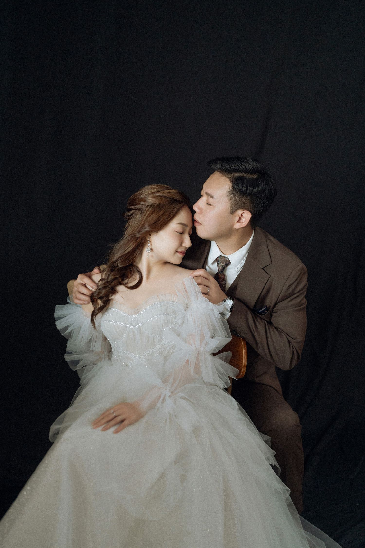 Intimate wedding portrait against black backdrop with dramatic lighting.