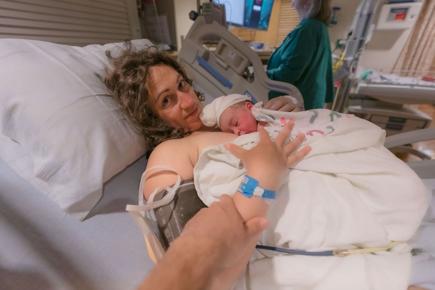 New parent holds newborn baby skin-to-skin in hospital recovery room after birth. In Santa Cruz, CA.