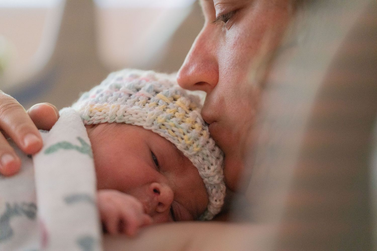 A tiny newborn wearing a knit hat being tenderly kissed.