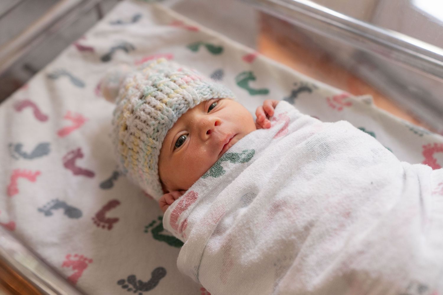 A newborn baby wearing a knit hat lying in a hospital bassinet. In Santa Cruz, CA.