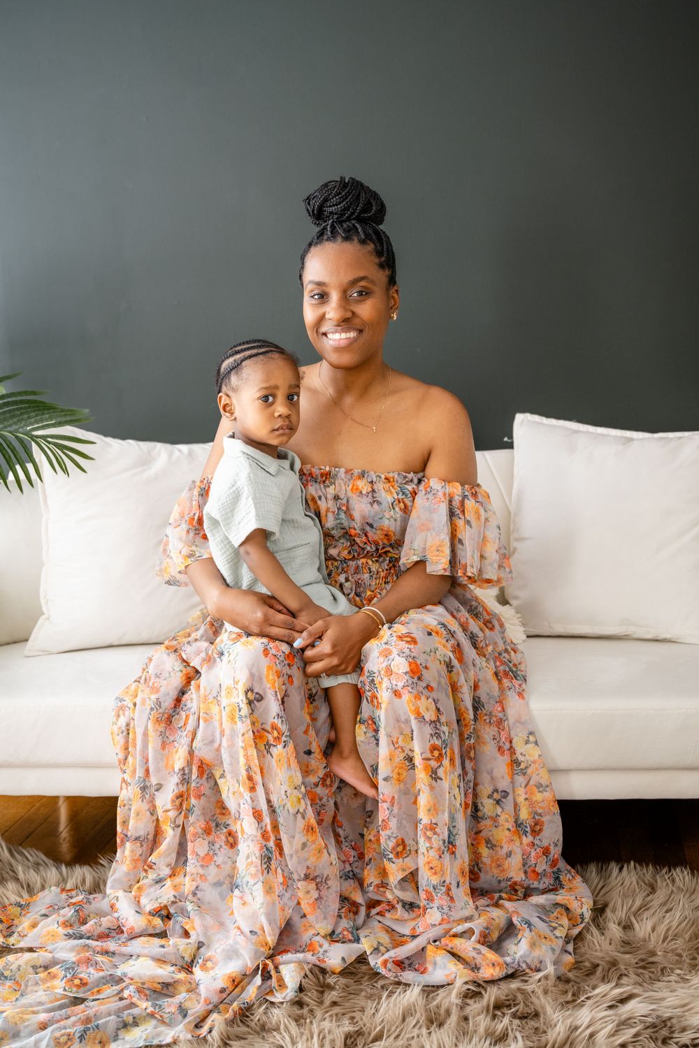 Intimate indoor portrait showing loving embrace on white couch, wearing floral dress.