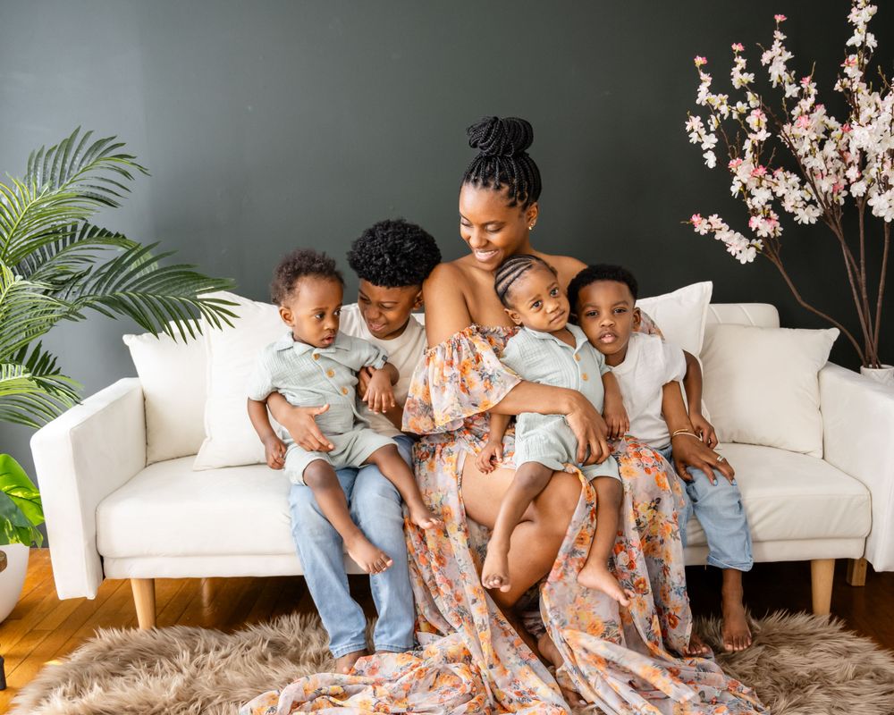 Family gathering on white sofa with floral dress against dark wall with decorative plants.