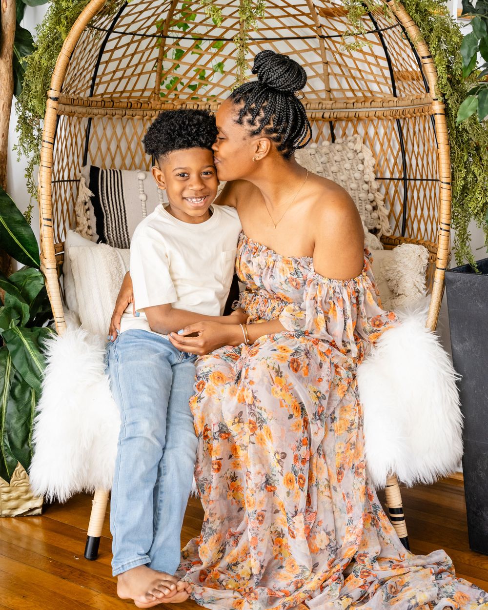 Happy moment shared in rattan egg chair with floral dress against natural decor.