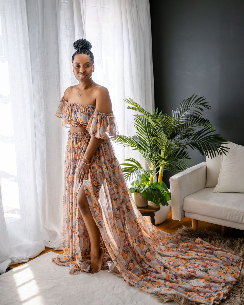 Floral off-shoulder maxi dress with dramatic train photographed against white curtains and indoor plants.