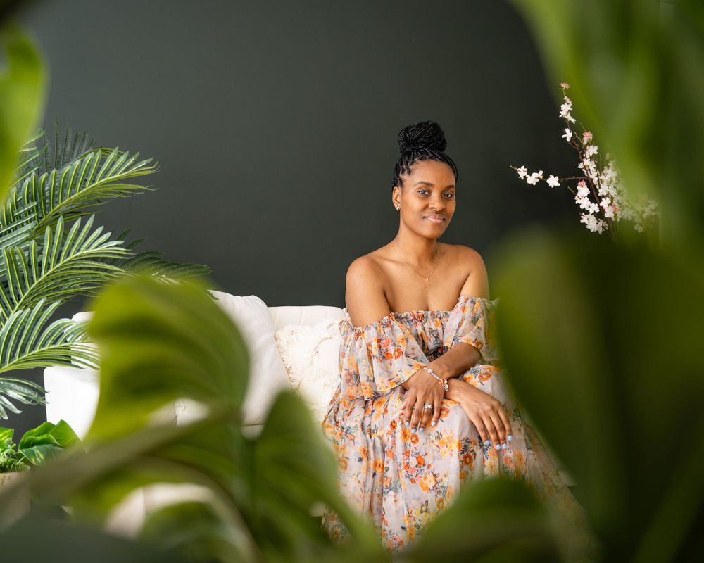 Tropical-themed portrait session with palm leaves and white floral accents against dark wall.