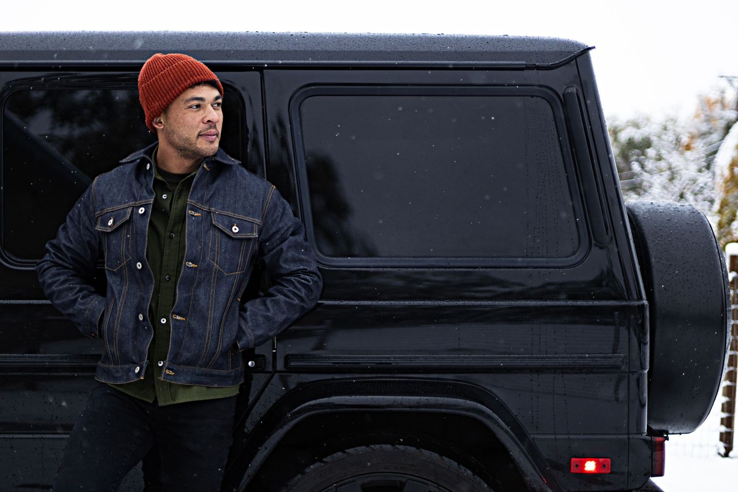 Person in winter attire standing next to a black Mercedes G-Class.