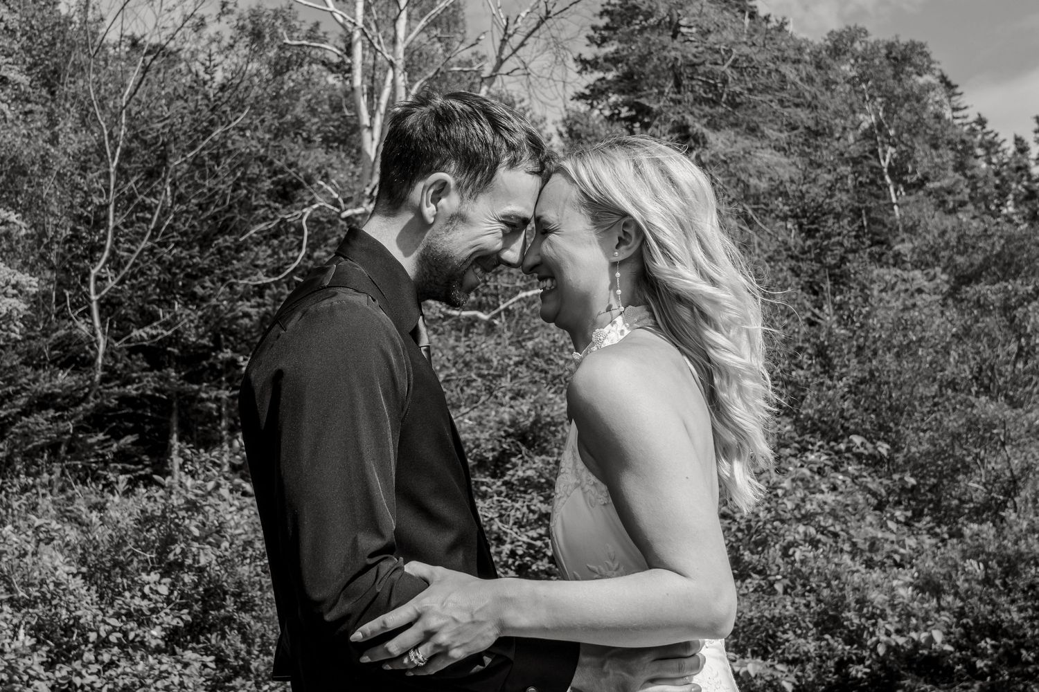 A romantic black and white moment between a couple embracing outdoors with trees and foliage in the background.