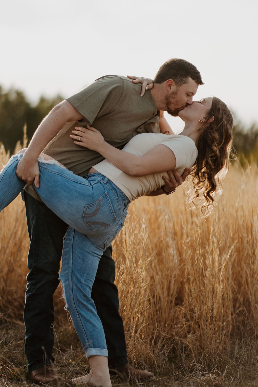 Romantic couple embraces and kisses in a golden wheat field during sunset.