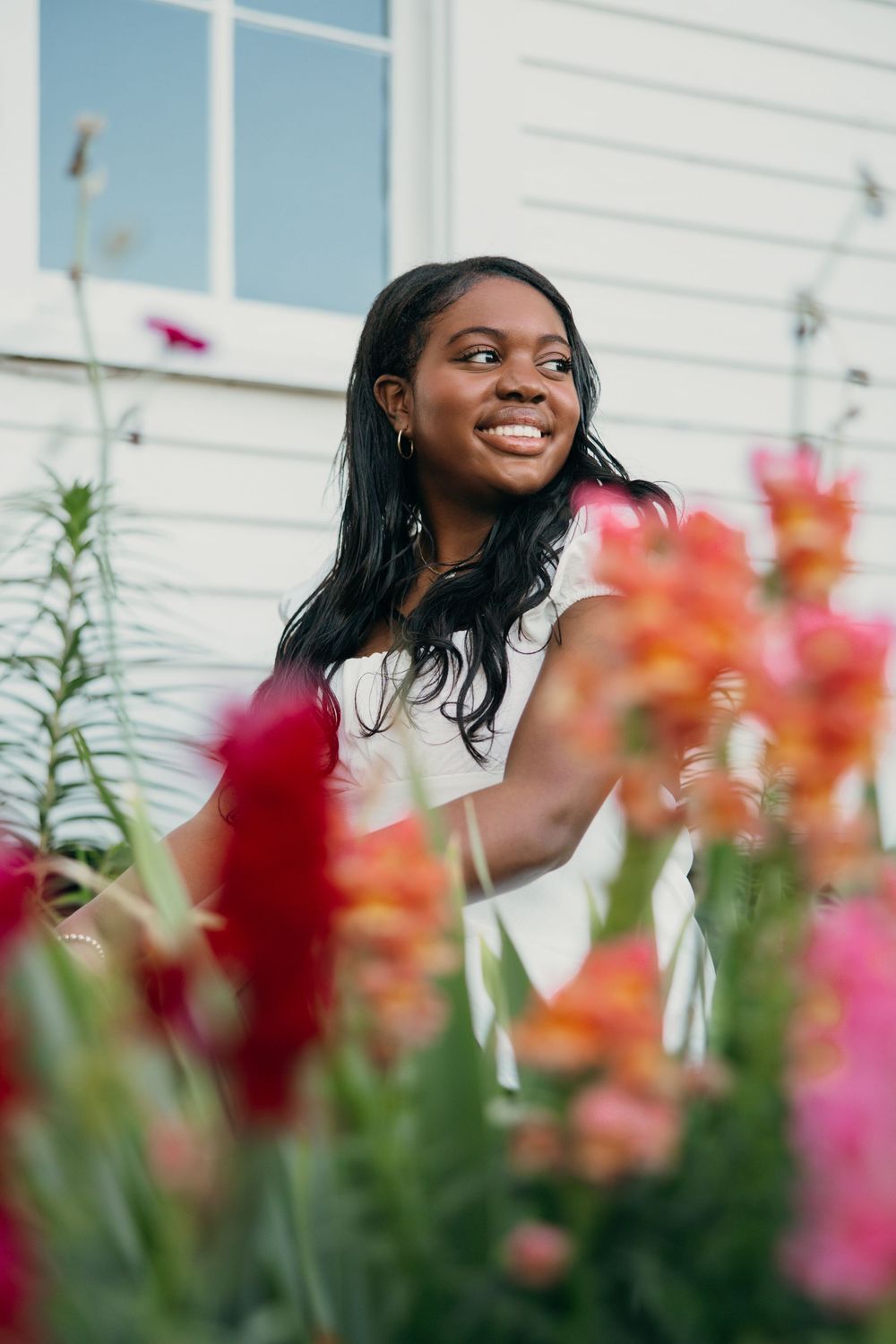 A joyful senior graduate smiling in a garden with vibrant red and orange flowers in the foreground.