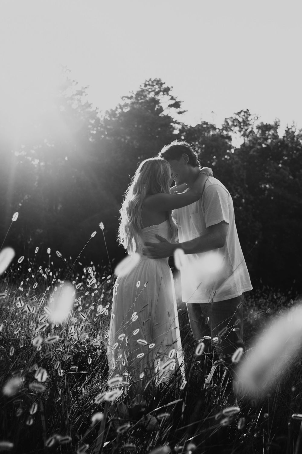 A romantic black and white photograph of a couple embracing in a sunlit meadow filled with wildflowers.