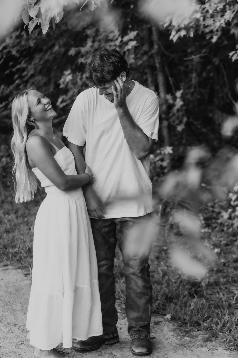A joyful black and white outdoor photo showing a couple laughing together on a nature path.