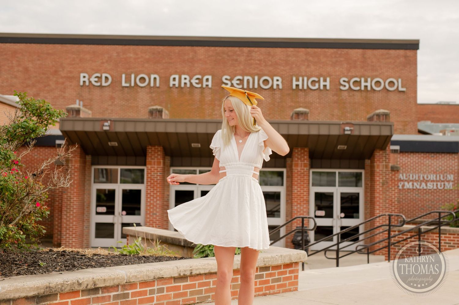 Graduate in white dress twirls outside Red Lion Area Senior High School entrance.
