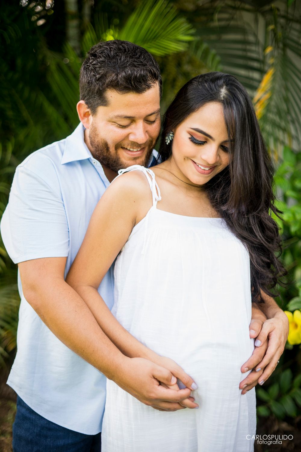 Intimate maternity moment captured in a lush tropical garden setting.