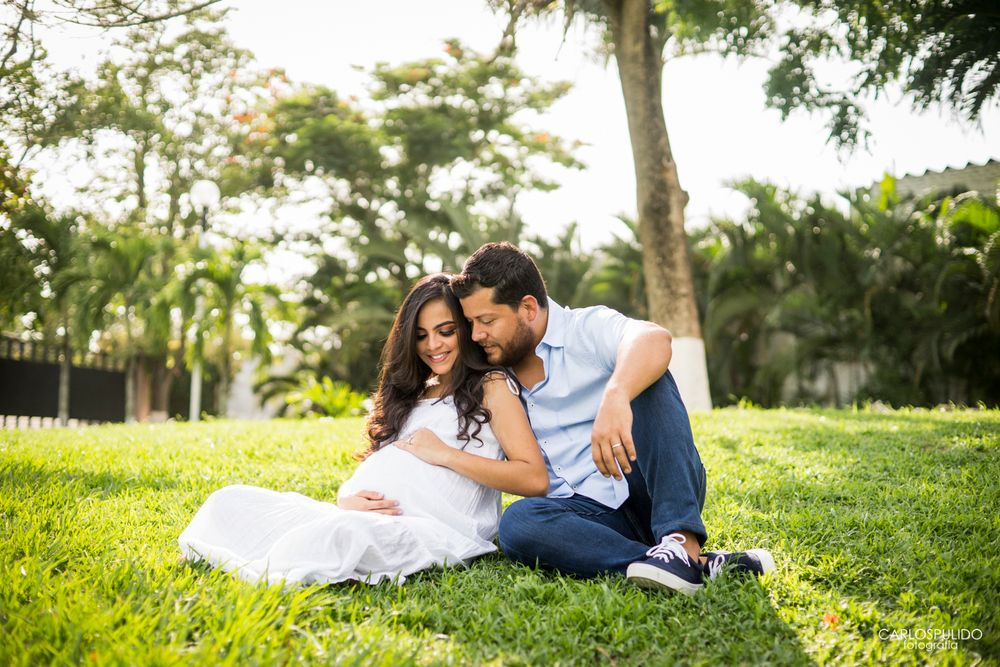 Intimate maternity portrait of couple sitting on grass in a sunlit garden setting.