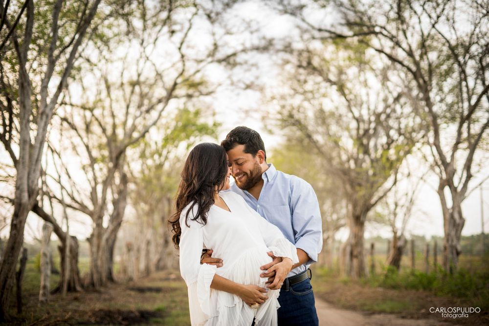 Romantic maternity photo of couple embracing on a tree-lined dirt path at sunset.