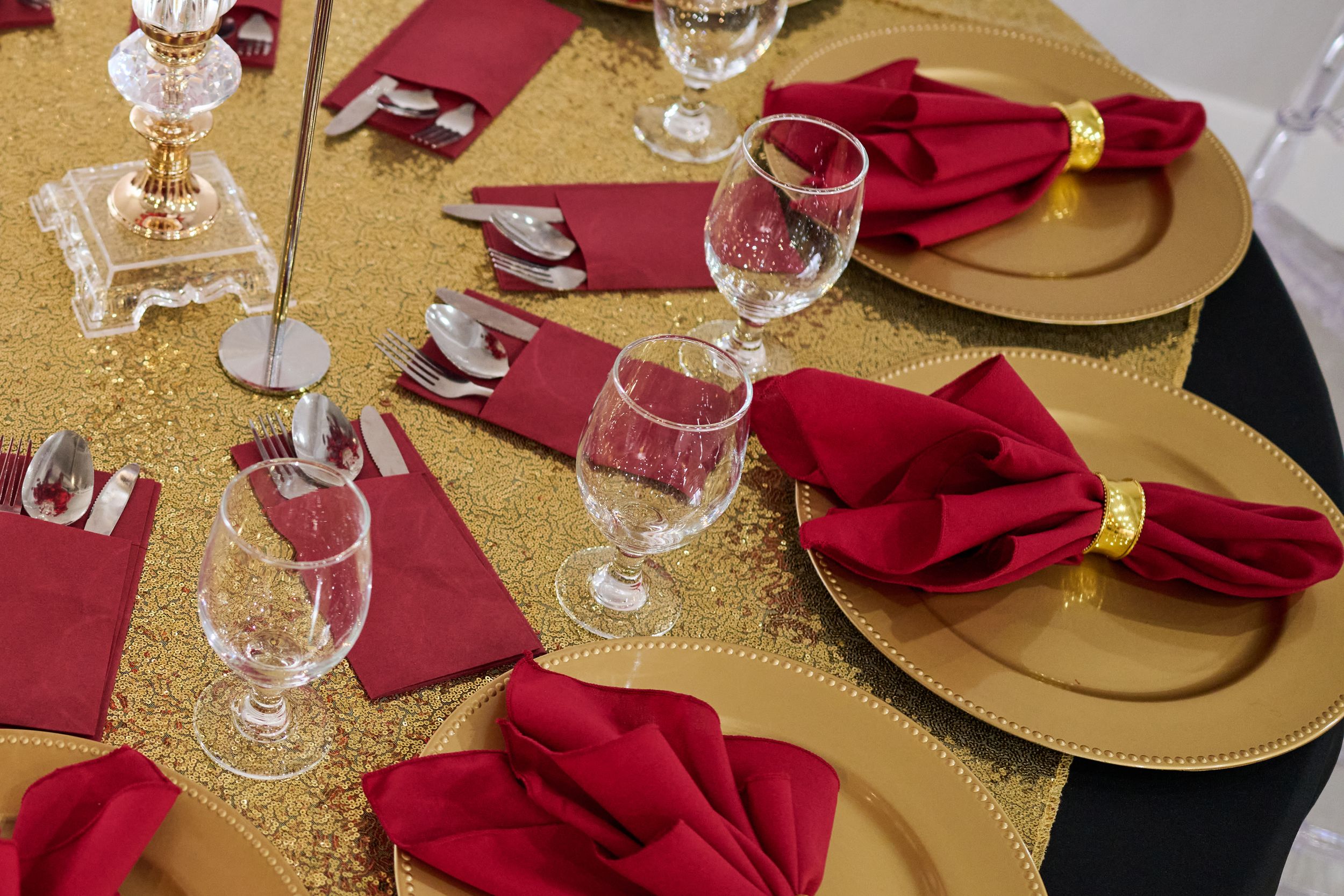 Elegant table setting with gold charger plates, red napkins, and crystal glasses on a sparkling gold tablecloth.