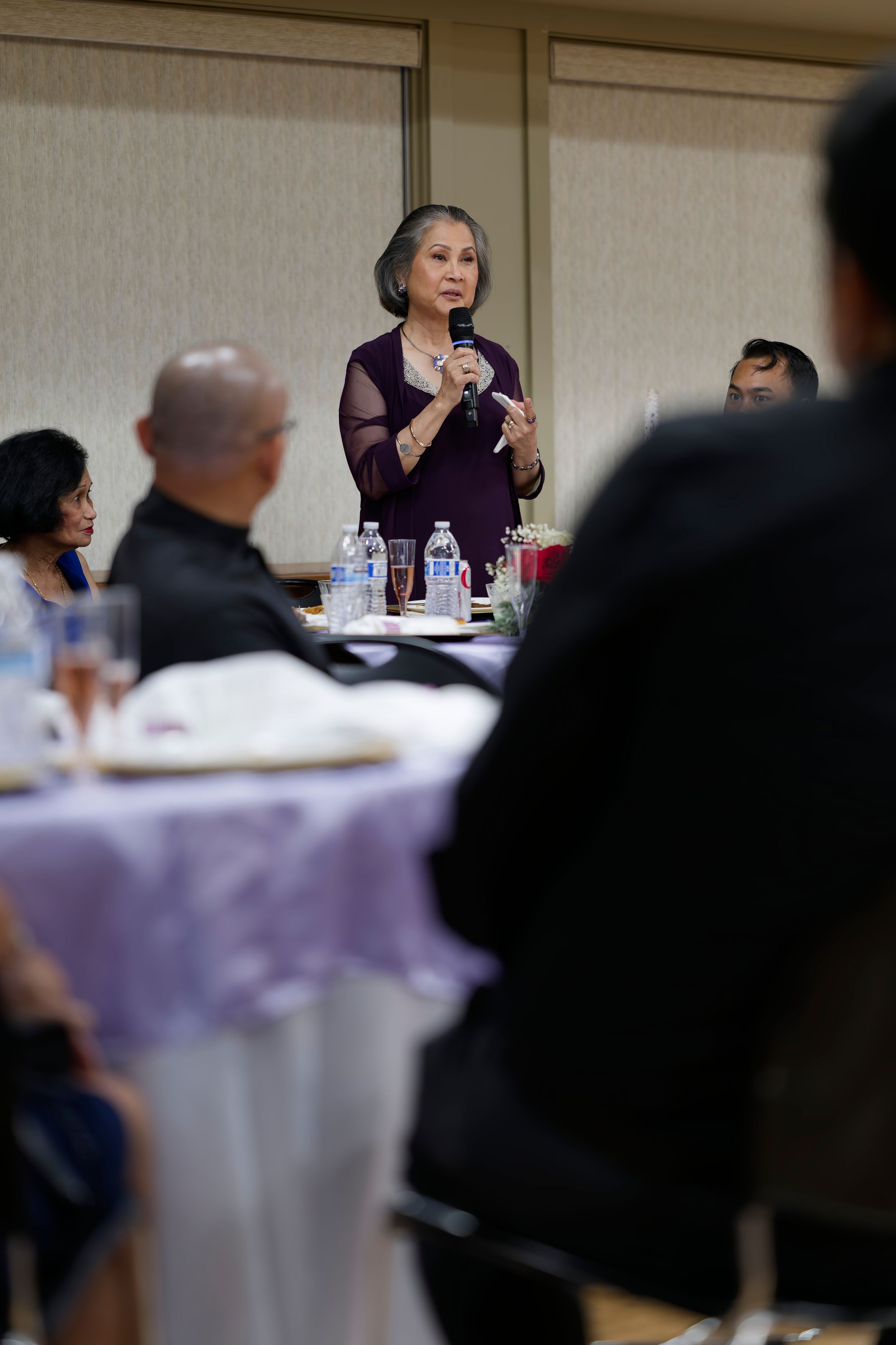 A speaker in a purple dress addresses attendees during a formal dinner event atSt. Bernadette's Catholic Church Hall in Stockton California.
