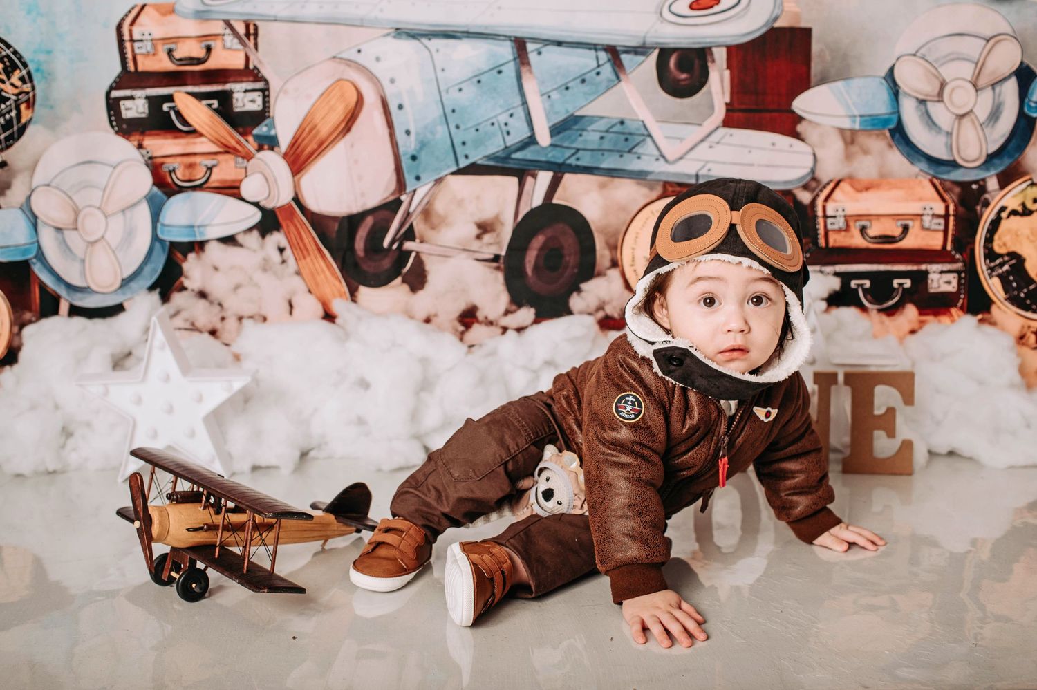 Vintage aviation themed photo setup with brown leather aviator costume, toy planes, and cloud-like cotton backdrops.