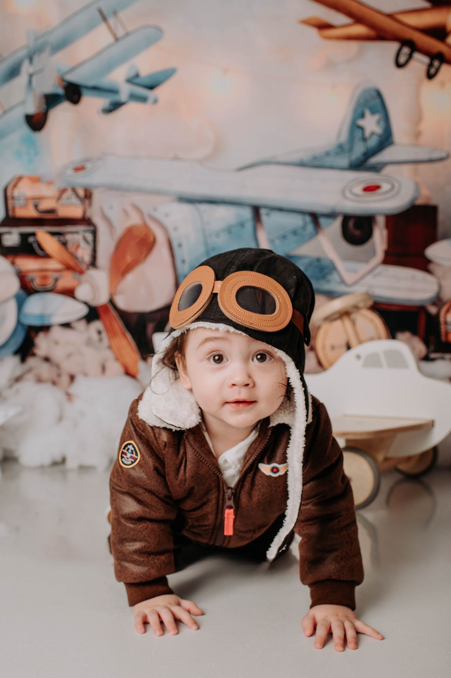 Retro aviation themed photo with brown leather aviator outfit against backdrop of vintage planes and suitcases.