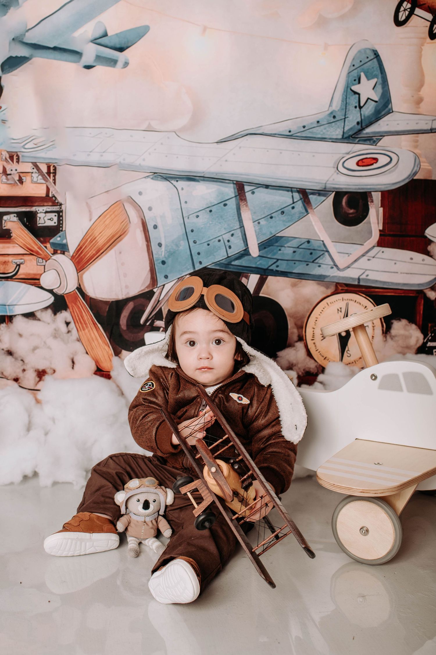 Aviation themed scene with stuffed koala, wooden toy plane, and vintage suitcases in background.