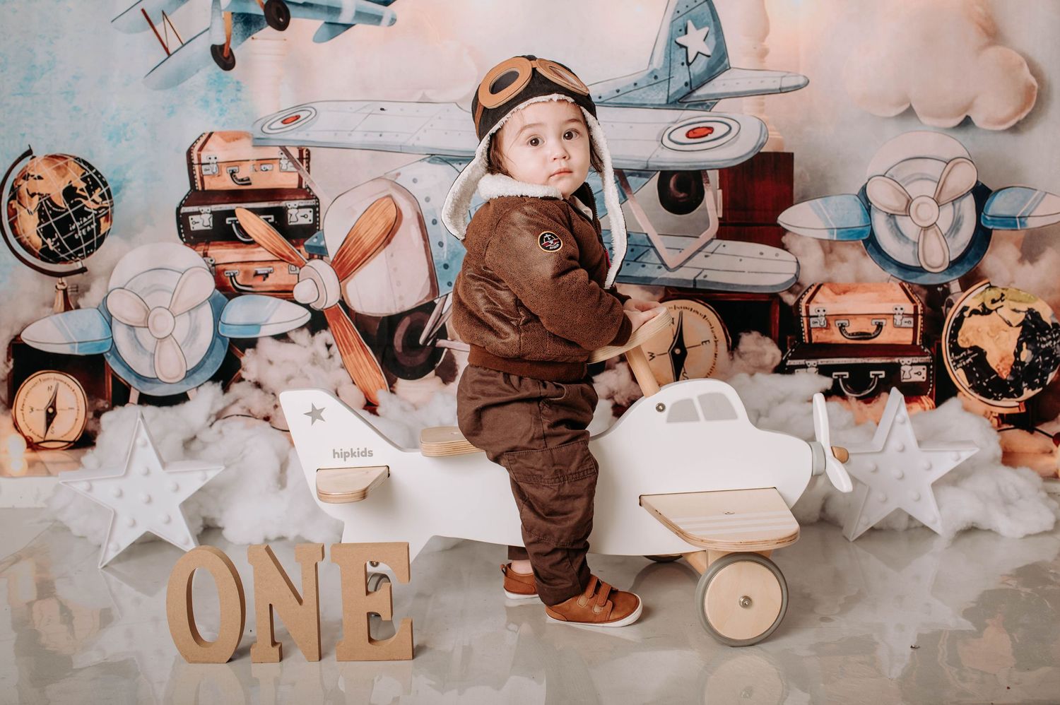 Aviation themed first birthday photo with wooden planes, vintage luggage, and cloud-like cotton backdrop.
