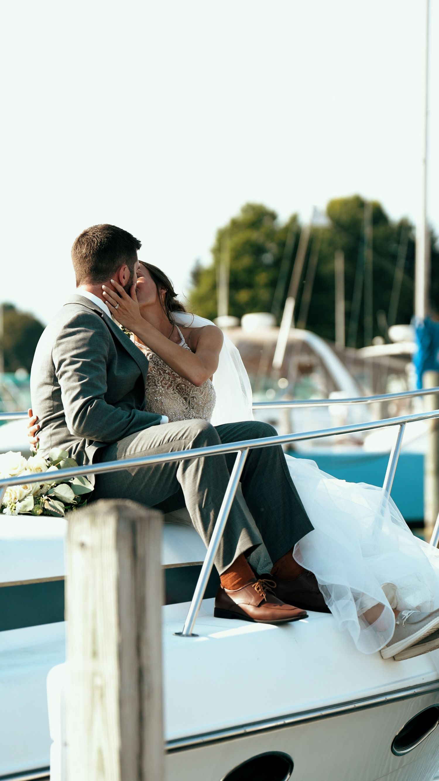 A romantic kiss between newlyweds on a boat dock with boats and marina in the background.