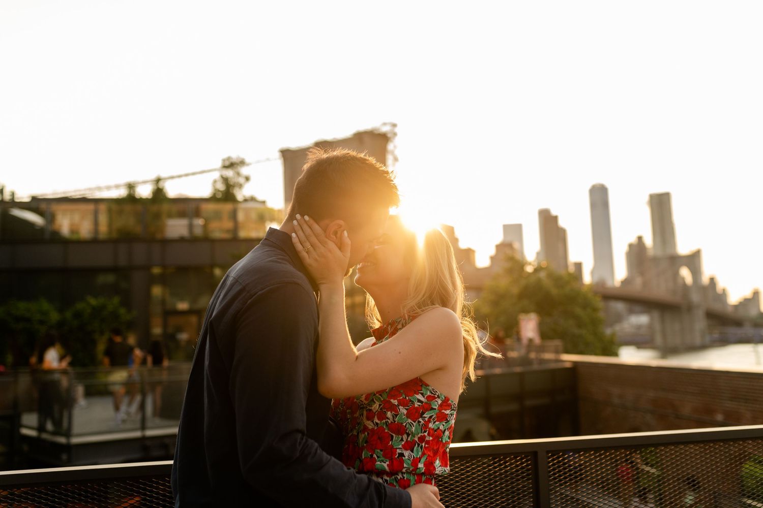 A romantic couple embraces on a rooftop terrace with a city skyline visible in the background.